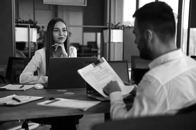 A woman attentively listens to a man discussing financial documents at a desk, symbolizing questions to ask a CPA.
