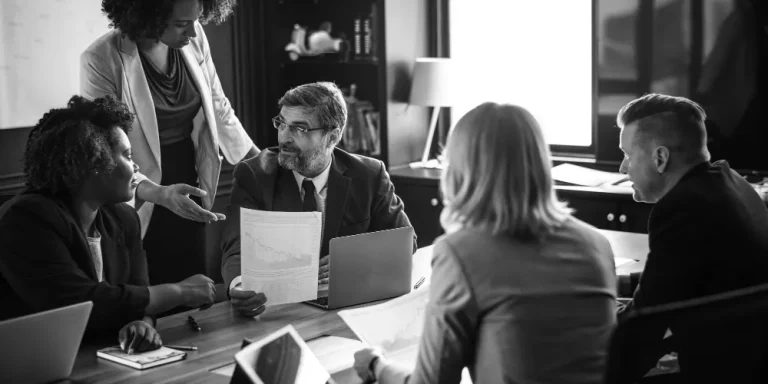A group of business professionals in a meeting room discuss a financial document related to a backdoor Roth IRA strategy.