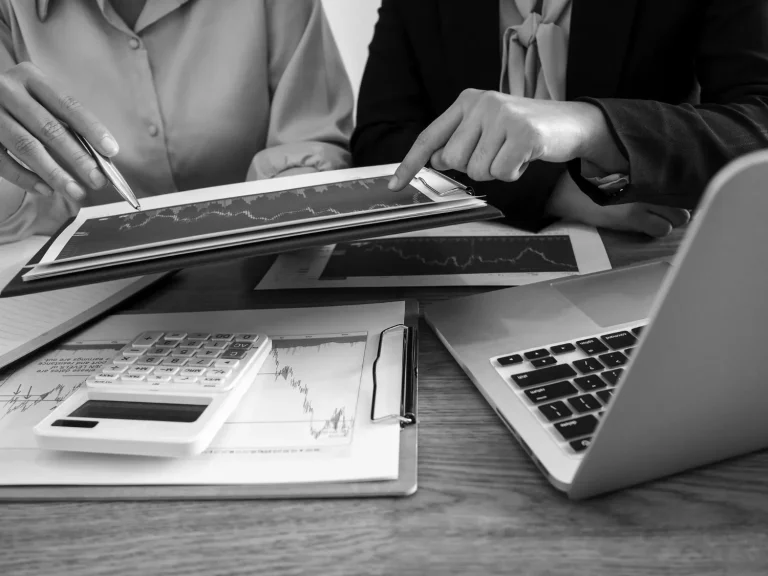 Two people discuss financial graphs and charts during a tax planning session, with a calculator and a laptop on the table.