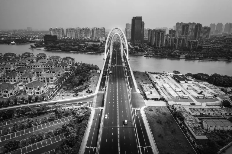 A monochrome aerial view of a cityscape with a prominent bridge, river, and surrounding residential and commercial properties, illustrating aspects of rental property depreciation.