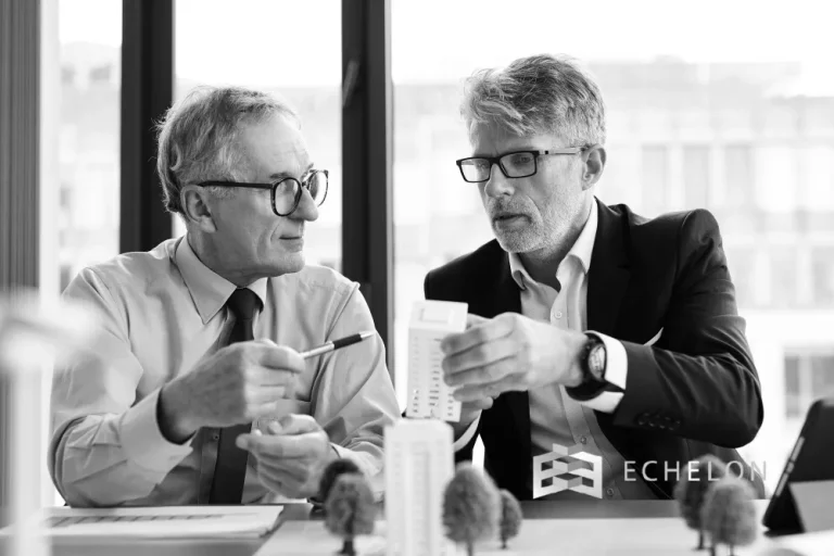Two men are engaged in a discussion while examining a small architectural model related to 351 Exchange, with the Echelon logo visible in the corner.