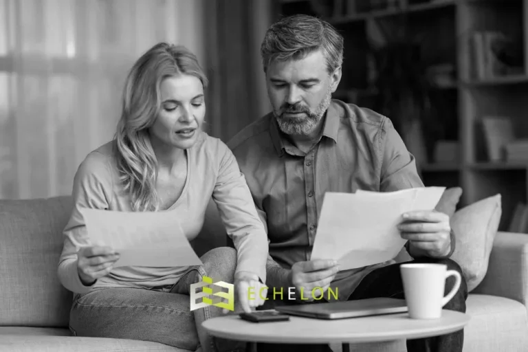 A couple sits on a couch reviewing beneficiary designation documents, with papers in hand and a coffee cup on the table.