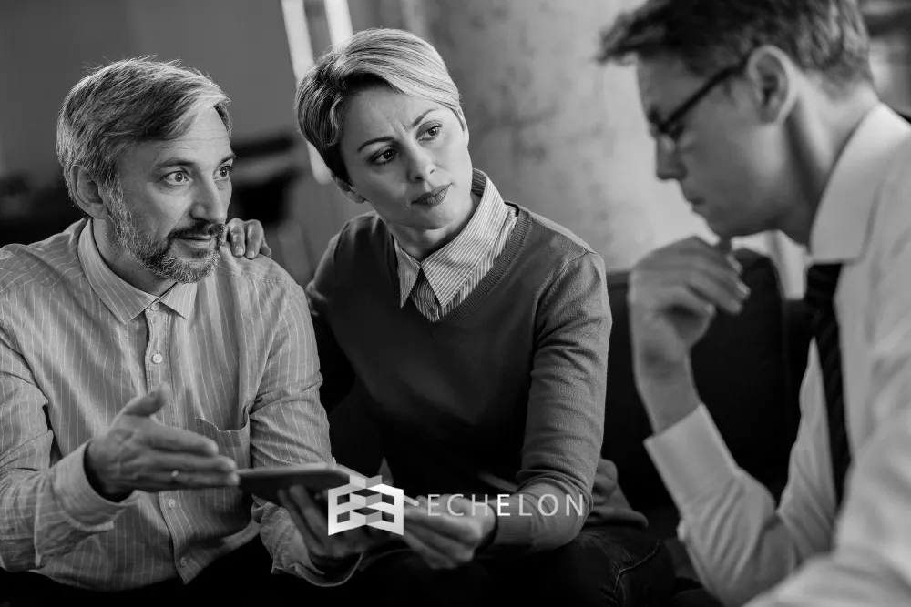 Three individuals engaged in a focused discussion, with one person pointing at a tablet, symbolizing strategic business exit planning.