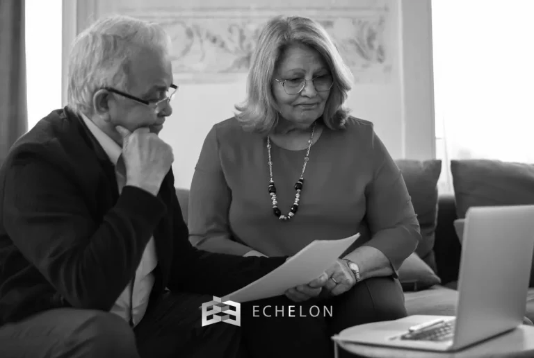 An older couple reviews retirement income documents together while seated in front of a laptop.