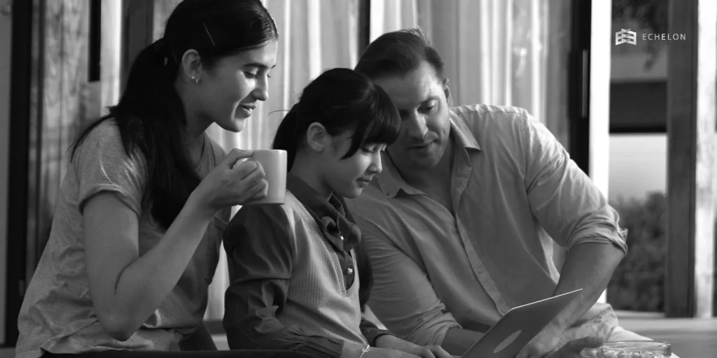 A high net worth financial advisor engages with a family, including a woman holding a mug and a young girl, while discussing information on a laptop.