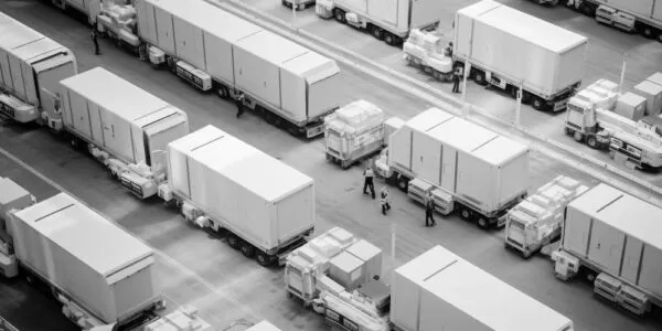 Rows of large trailers and semi-trucks are parked in an organized manner on paved surfaces, with a few people walking between them.