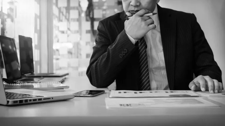 A person in a suit sits at a desk reviewing financial documents and charts, surrounded by laptops, reflecting on business valuation methods.