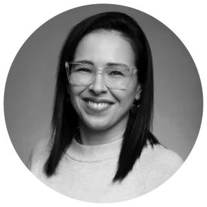 Woman with long dark hair wearing glasses and smiling, in a grayscale portrait.