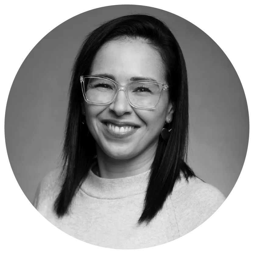 Woman with long dark hair wearing glasses and smiling, in a grayscale portrait.