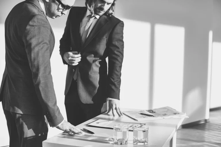 Two men in suits examine documents on a table, symbolizing considerations for choosing an accountant.