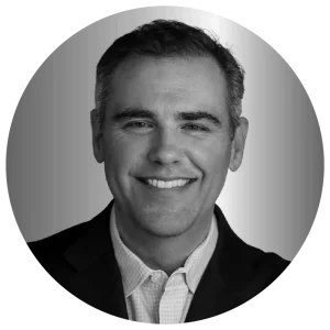 Smiling man in a suit and collared shirt in a grayscale circular frame.