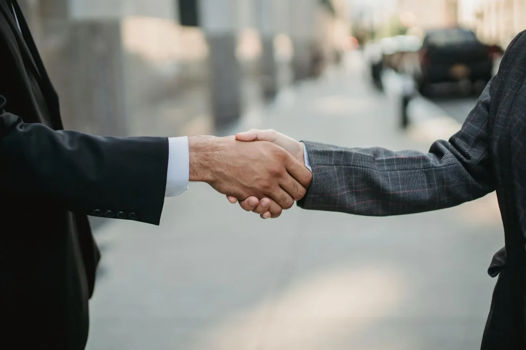 Two people in business attire shake hands outdoors, symbolizing a successful business exit planning agreement.