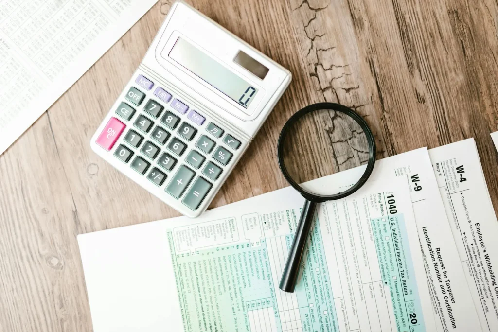 A calculator, magnifying glass, and tax forms on a wooden table, symbolizing tax planning and high net worth wealth management.